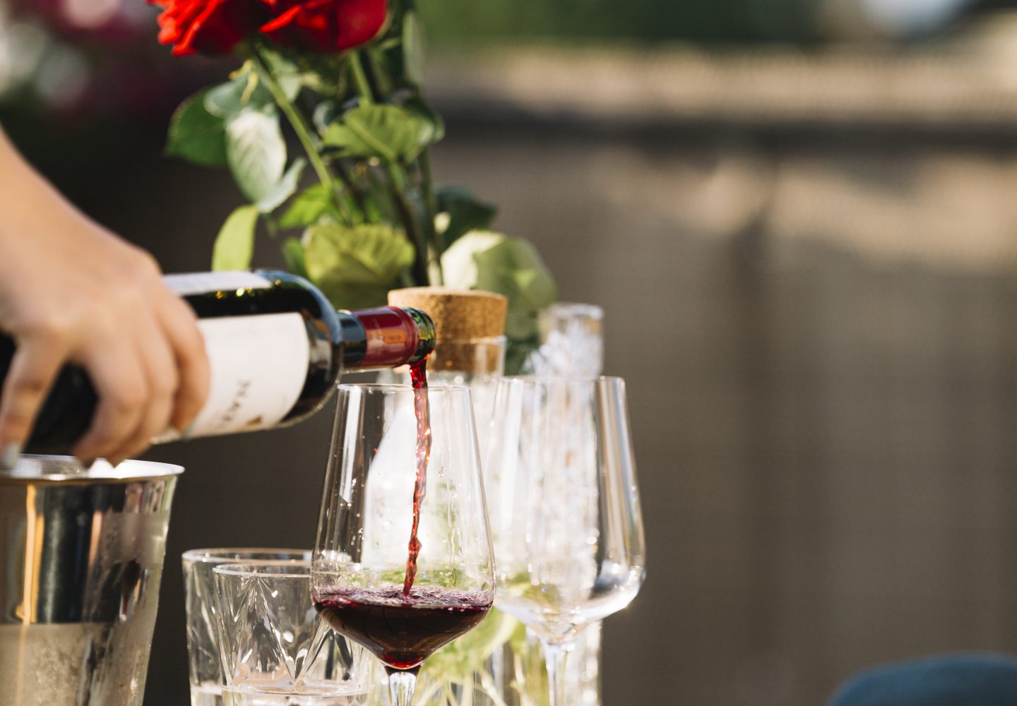 close-up-hand-pouring-wine-transparent-glass-wooden-table