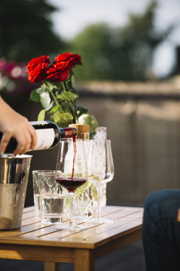 close-up-hand-pouring-wine-transparent-glass-wooden-table
