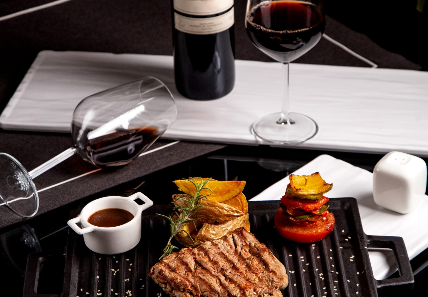 steak served with potatoes grilled vegetables sauce and wine
