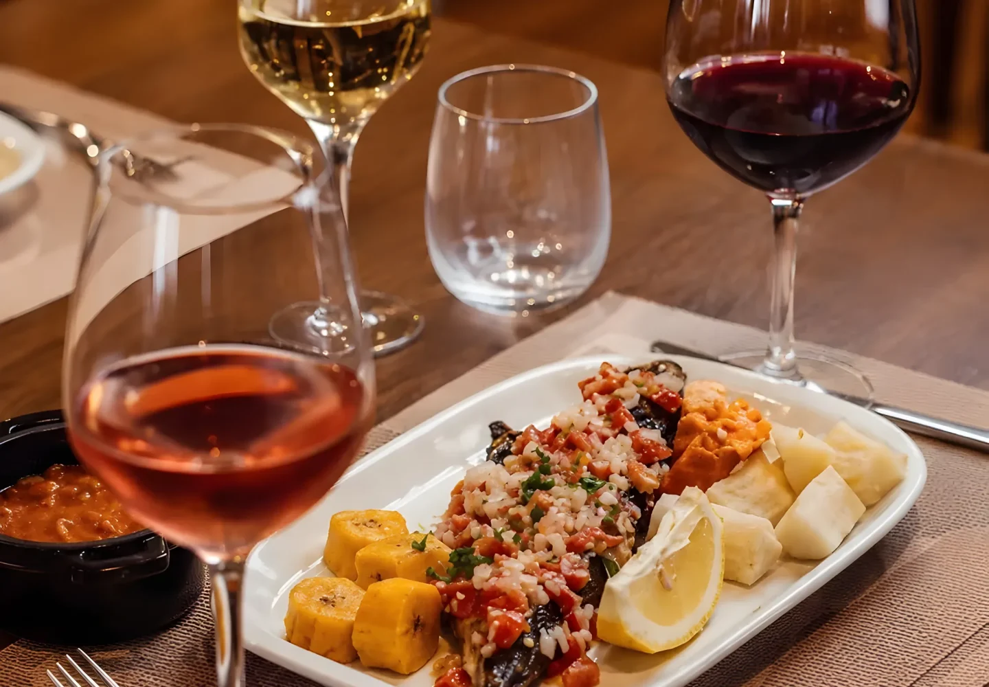 O Mufete Angolano Grelhado, com funge e banana-pão, harmonizado com três taças de vinho (rosé, branco e tinto) em uma mesa de restaurante, com tags educativas de harmonização para comida angolana.