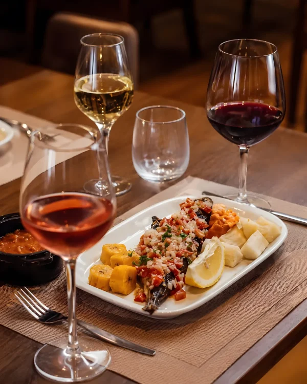 O Mufete Angolano Grelhado, com funge e banana-pão, harmonizado com três taças de vinho (rosé, branco e tinto) em uma mesa de restaurante, com tags educativas de harmonização para comida angolana.